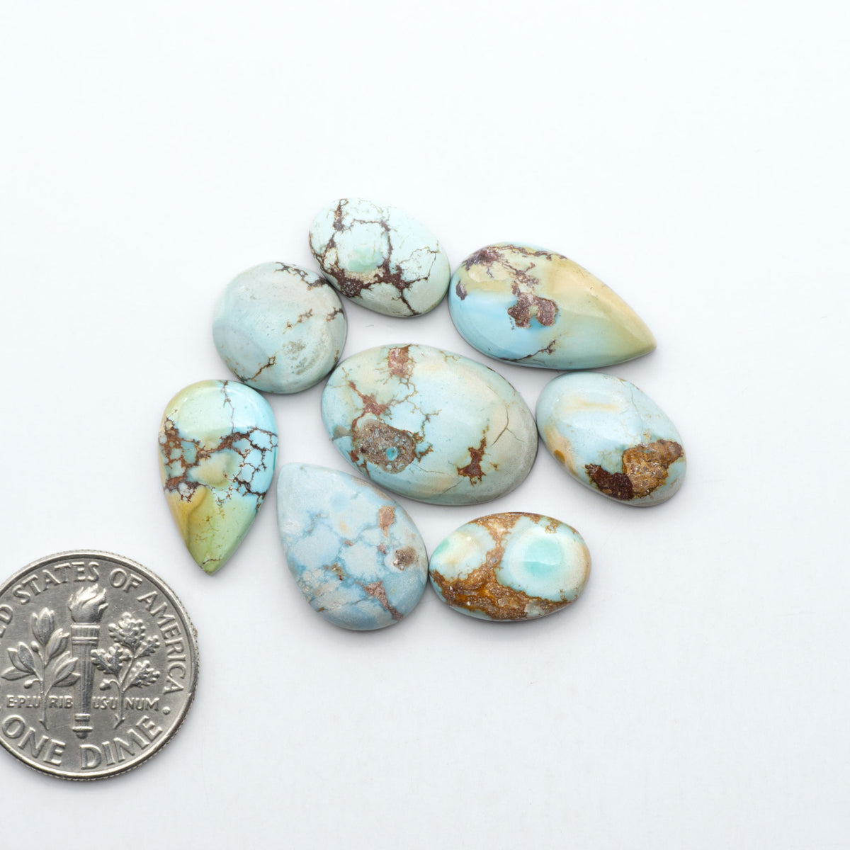 Golden Hills Turquoise cabochons, icy blue to lavender tones with chocolate matrix, polished stones on a white background with a US dime for scale