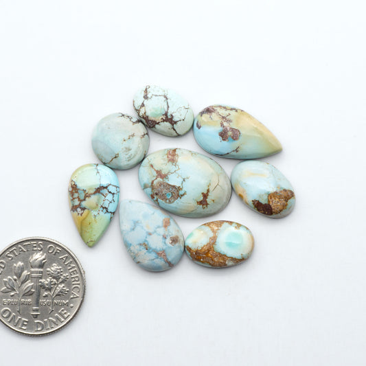 Golden Hills Turquoise cabochons, icy blue to lavender tones with chocolate matrix, polished stones on a white background with a US dime for scale