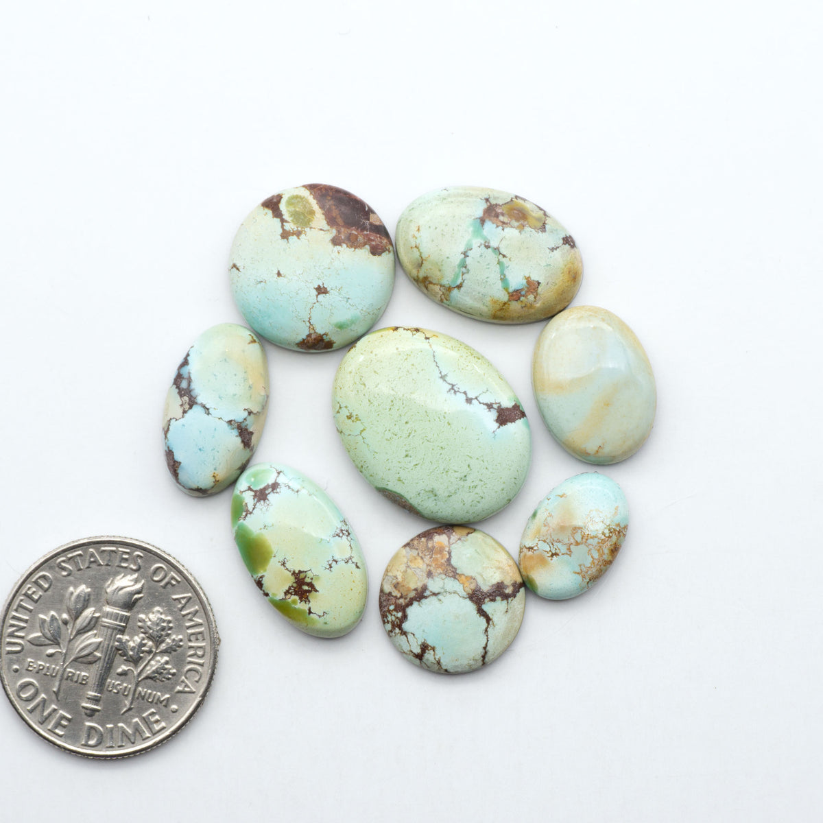 Golden Hills Turquoise cabochons, icy blue to lavender tones with chocolate matrix, polished stones on a white background with a US dime for scale
