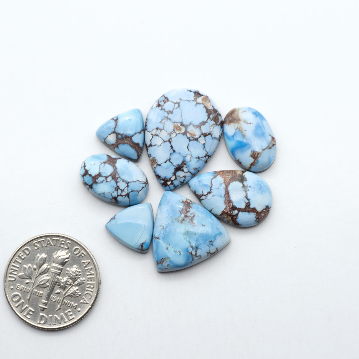 Golden Hills Turquoise cabochons, icy blue to lavender tones with chocolate matrix, polished stones on a white background with a US dime for scale