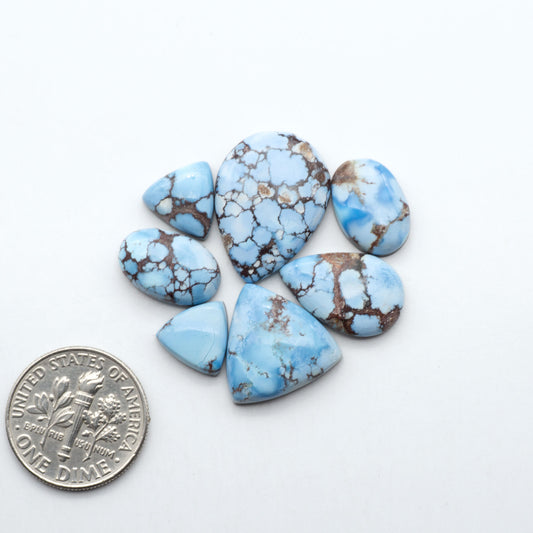 Golden Hills Turquoise cabochons, icy blue to lavender tones with chocolate matrix, polished stones on a white background with a US dime for scale