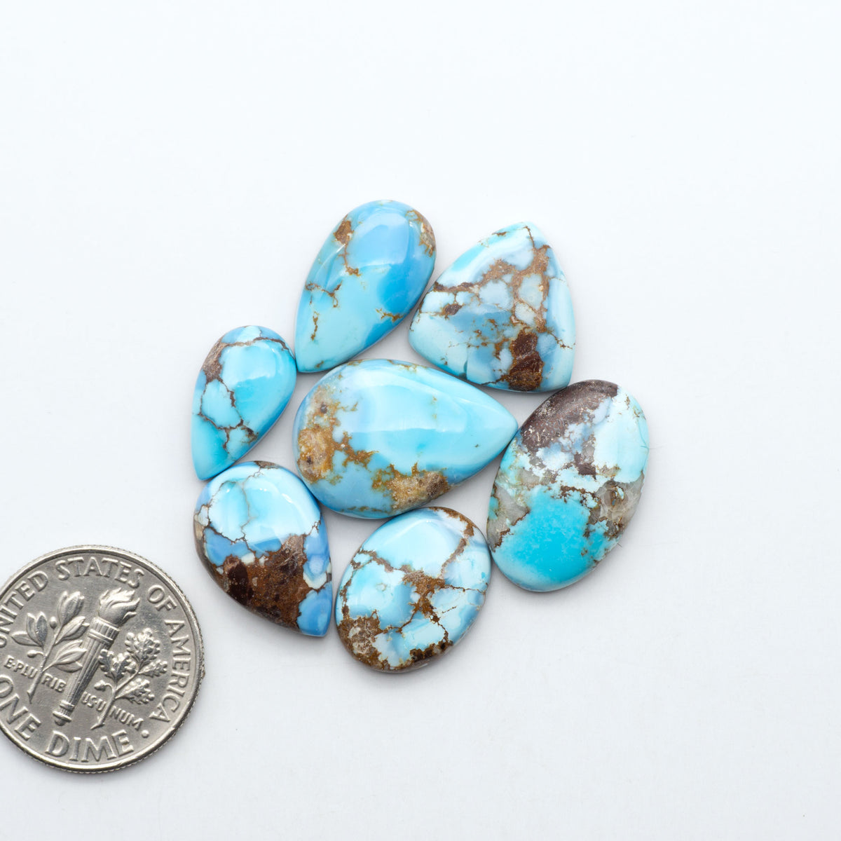 Golden Hills Turquoise cabochons, icy blue to lavender tones with chocolate matrix, polished stones on a white background with a US dime for scale