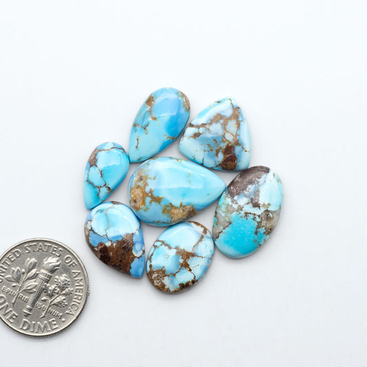 Golden Hills Turquoise cabochons, icy blue to lavender tones with chocolate matrix, polished stones on a white background with a US dime for scale