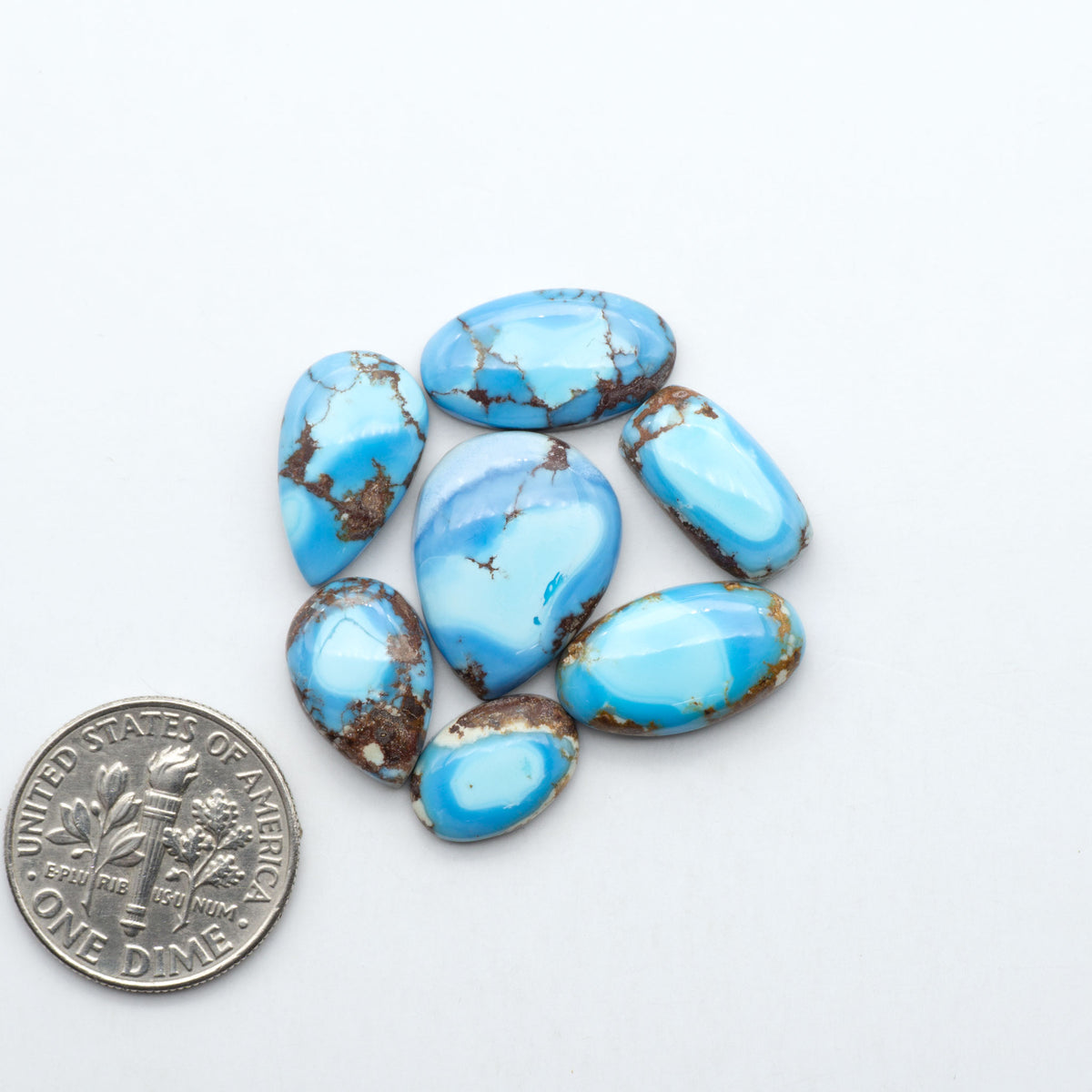 Golden Hills Turquoise cabochons, icy blue to lavender tones with chocolate matrix, polished stones on a white background with a US dime for scale