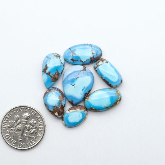 Golden Hills Turquoise cabochons, icy blue to lavender tones with chocolate matrix, polished stones on a white background with a US dime for scale