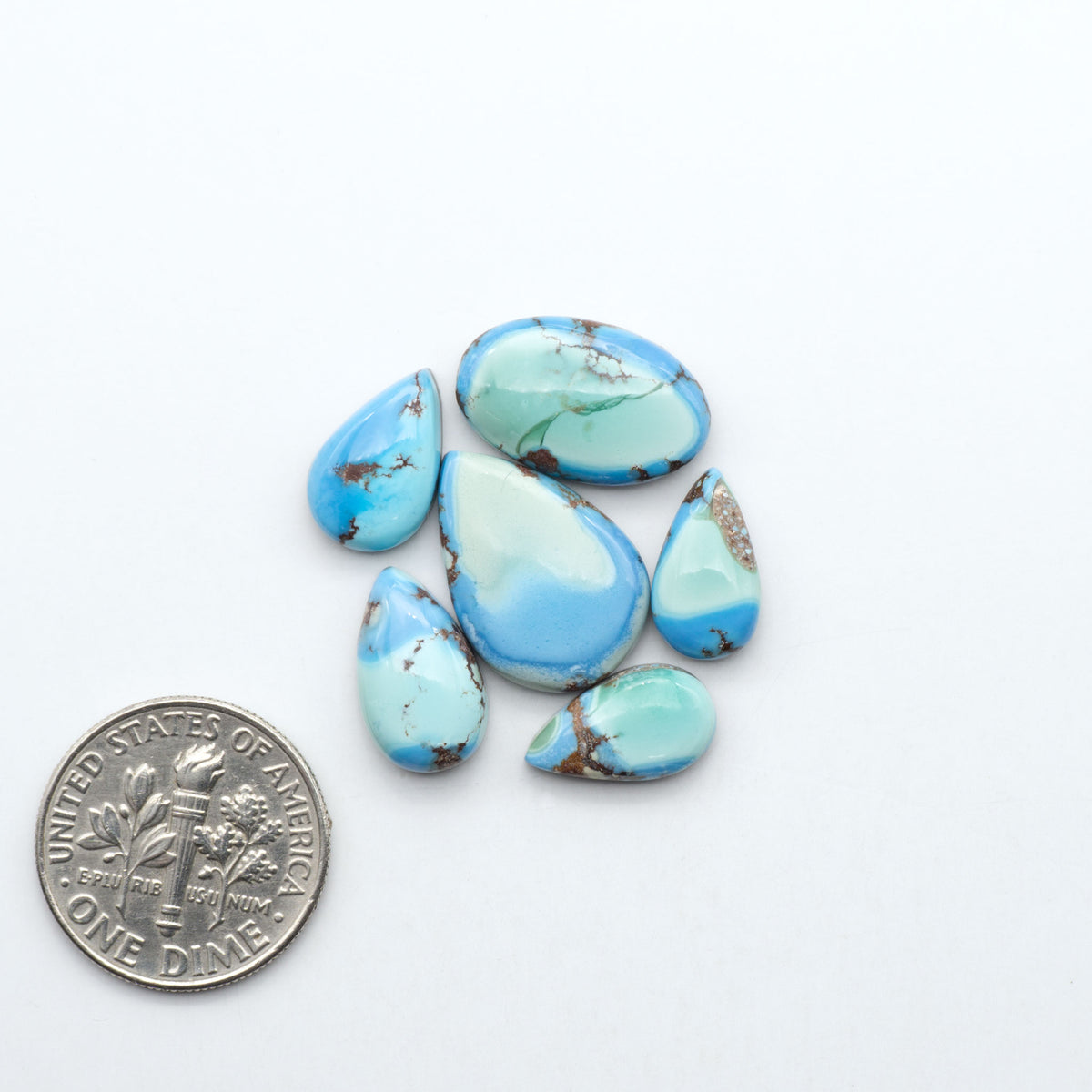 Golden Hills Turquoise cabochons, icy blue to lavender tones with chocolate matrix, polished stones on a white background with a US dime for scale