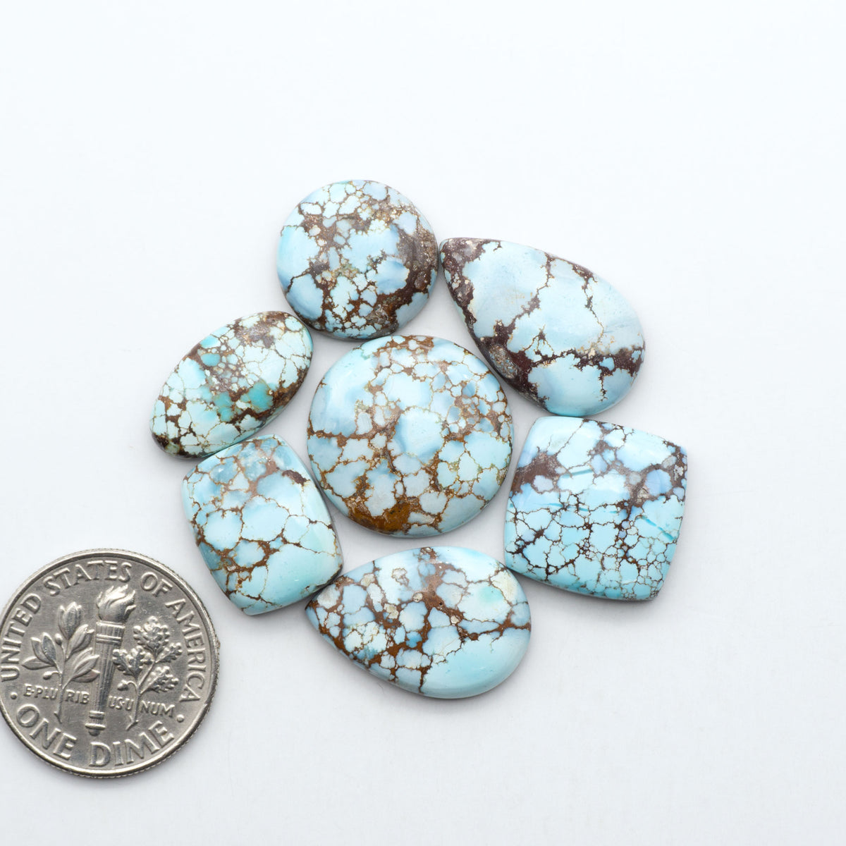 Golden Hills Turquoise cabochons, icy blue to lavender tones with chocolate matrix, polished stones on a white background with a US dime for scale