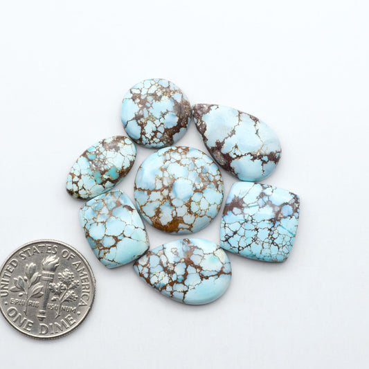 Golden Hills Turquoise cabochons, icy blue to lavender tones with chocolate matrix, polished stones on a white background with a US dime for scale