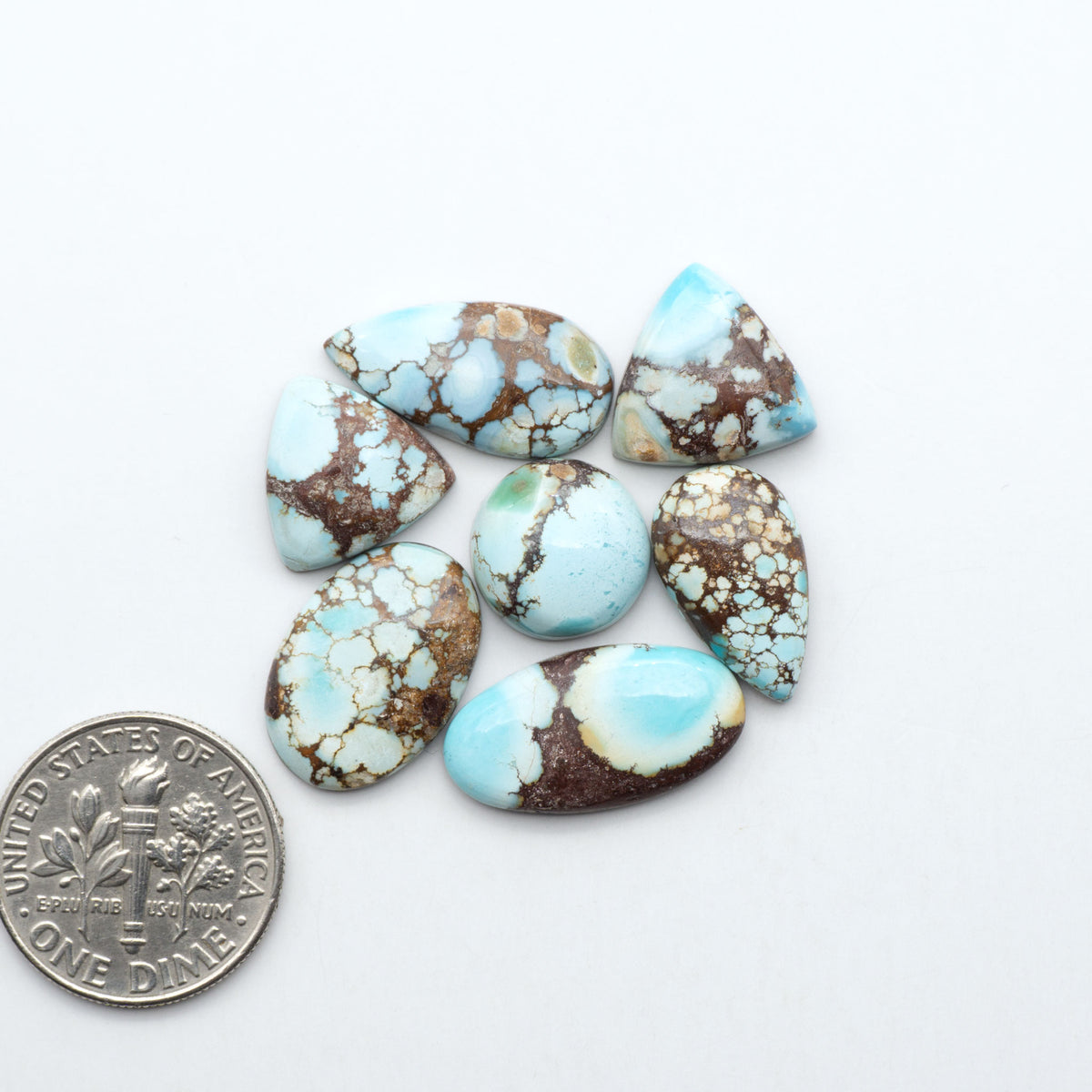 Golden Hills Turquoise cabochons, icy blue to lavender tones with chocolate matrix, polished stones on a white background with a US dime for scale