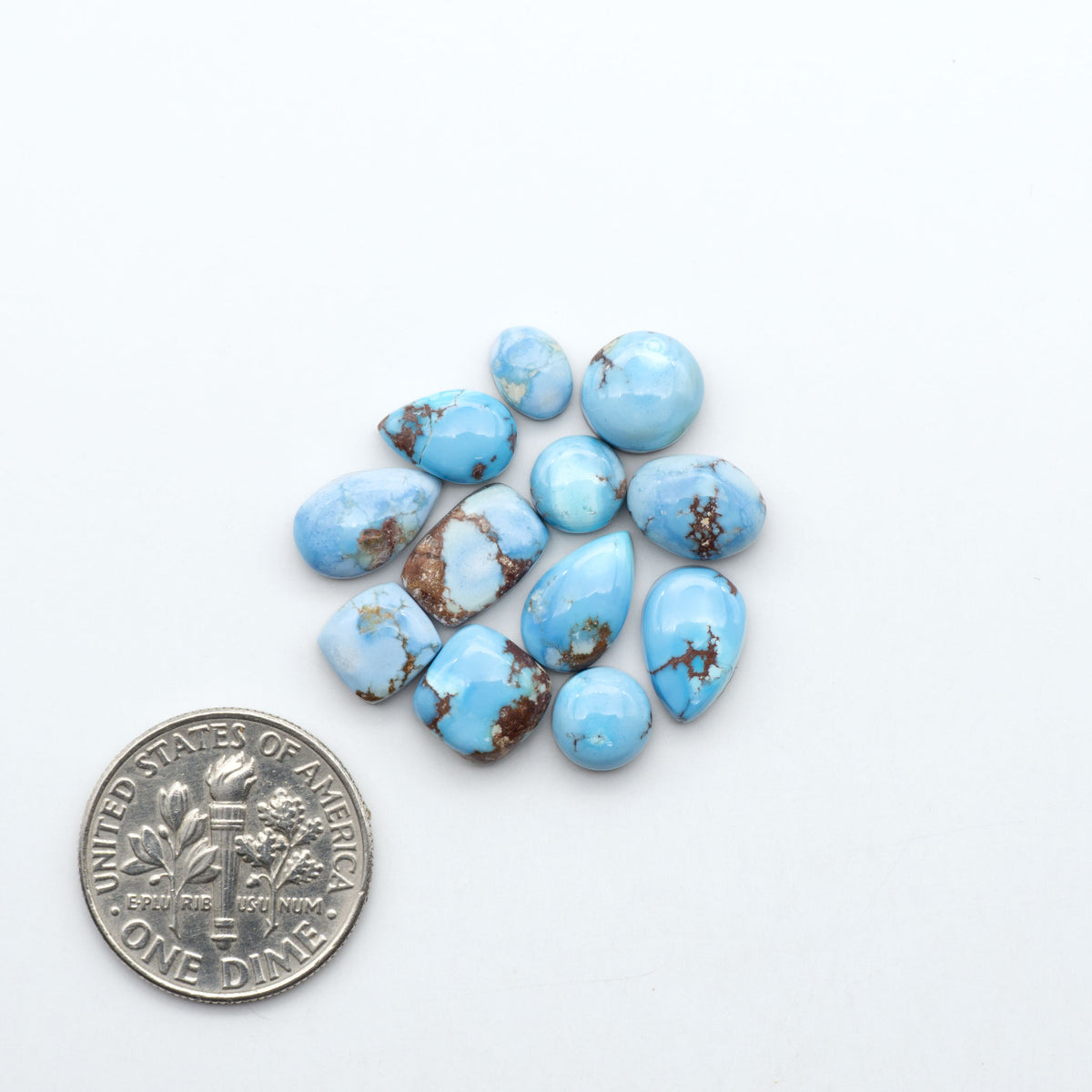Golden Hills Turquoise cabochons, icy blue to lavender tones with chocolate matrix, polished stones on a white background with a US dime for scale