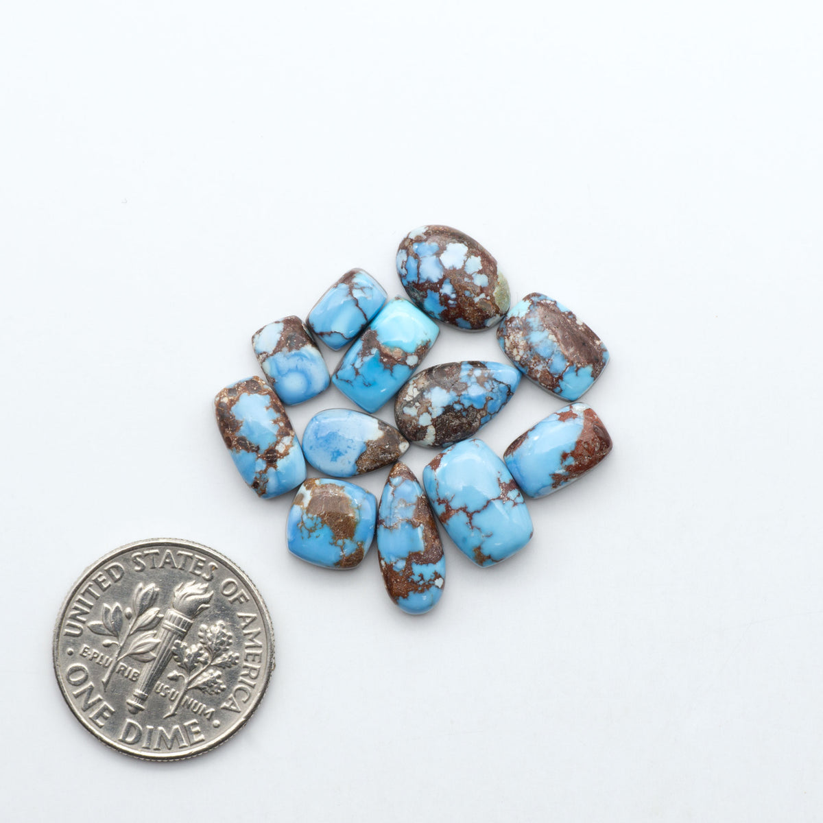 Golden Hills Turquoise cabochons, icy blue to lavender tones with chocolate matrix, polished stones on a white background with a US dime for scale