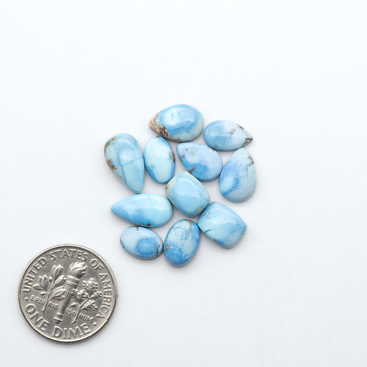 Golden Hills Turquoise cabochons, icy blue to lavender tones with chocolate matrix, polished stones on a white background with a US dime for scale