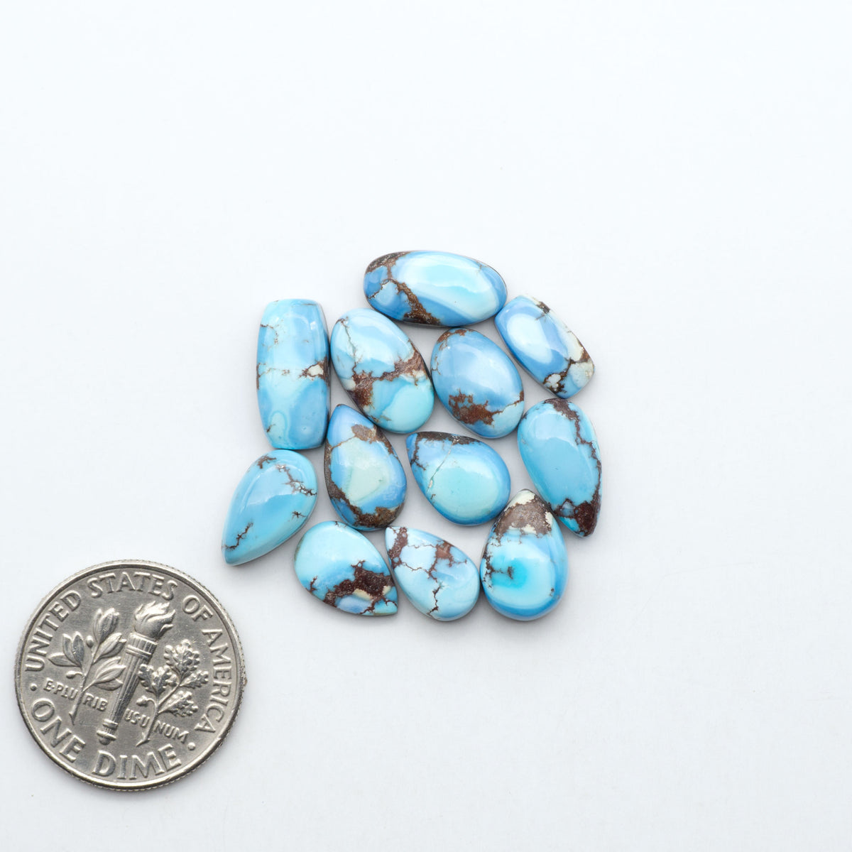Golden Hills Turquoise cabochons, icy blue to lavender tones with chocolate matrix, polished stones on a white background with a US dime for scale