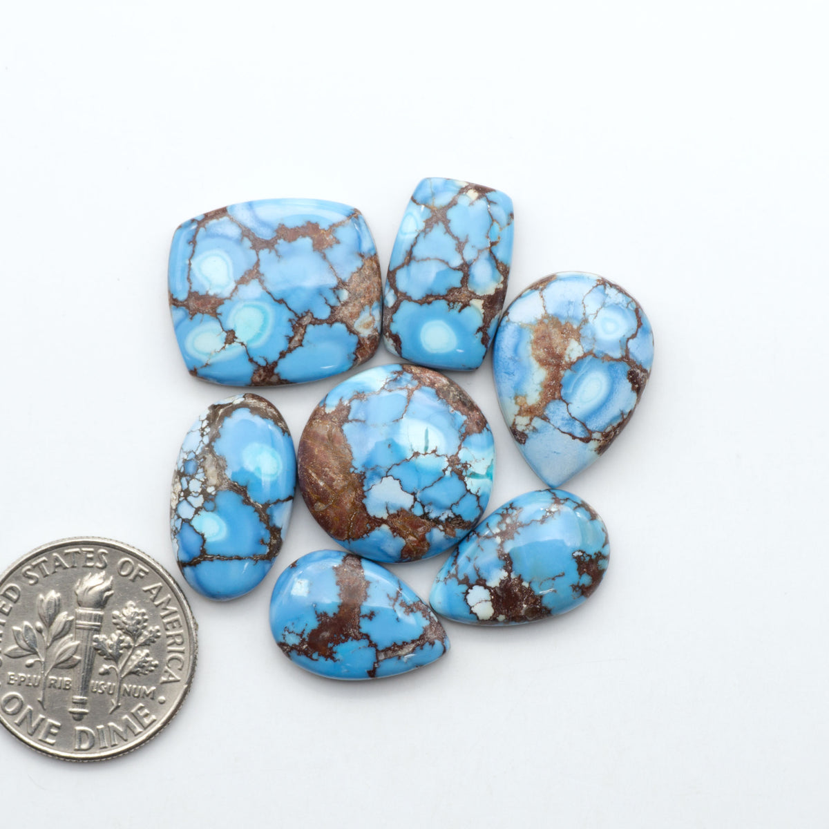 Golden Hills Turquoise cabochons, icy blue to lavender tones with chocolate matrix, polished stones on a white background with a US dime for scale