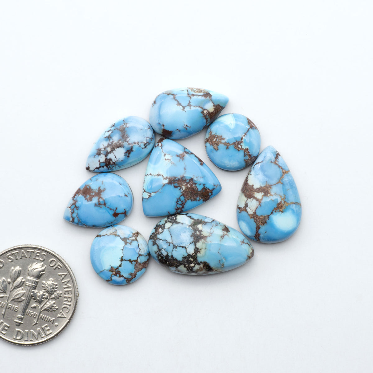 Golden Hills Turquoise cabochons, icy blue to lavender tones with chocolate matrix, polished stones on a white background with a US dime for scale
