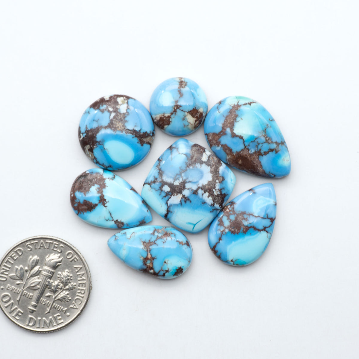 Golden Hills Turquoise cabochons, icy blue to lavender tones with chocolate matrix, polished stones on a white background with a US dime for scale