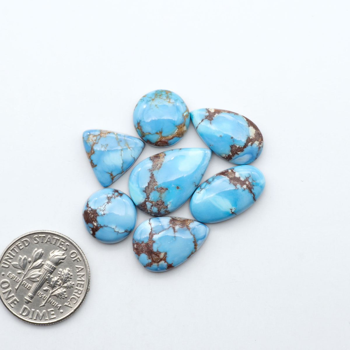 Golden Hills Turquoise cabochons, icy blue to lavender tones with chocolate matrix, polished stones on a white background with a US dime for scale