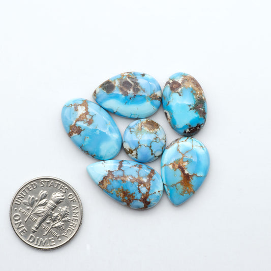 Golden Hills Turquoise cabochons, icy blue to lavender tones with chocolate matrix, polished stones on a white background with a US dime for scale
