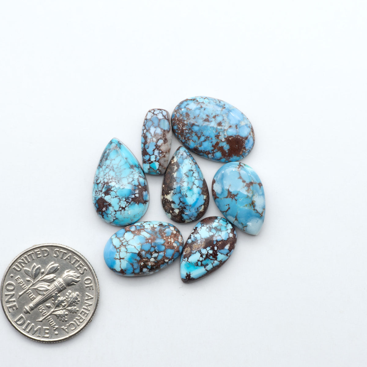 Golden Hills Turquoise cabochons, icy blue to lavender tones with chocolate matrix, polished stones on a white background with a US dime for scale