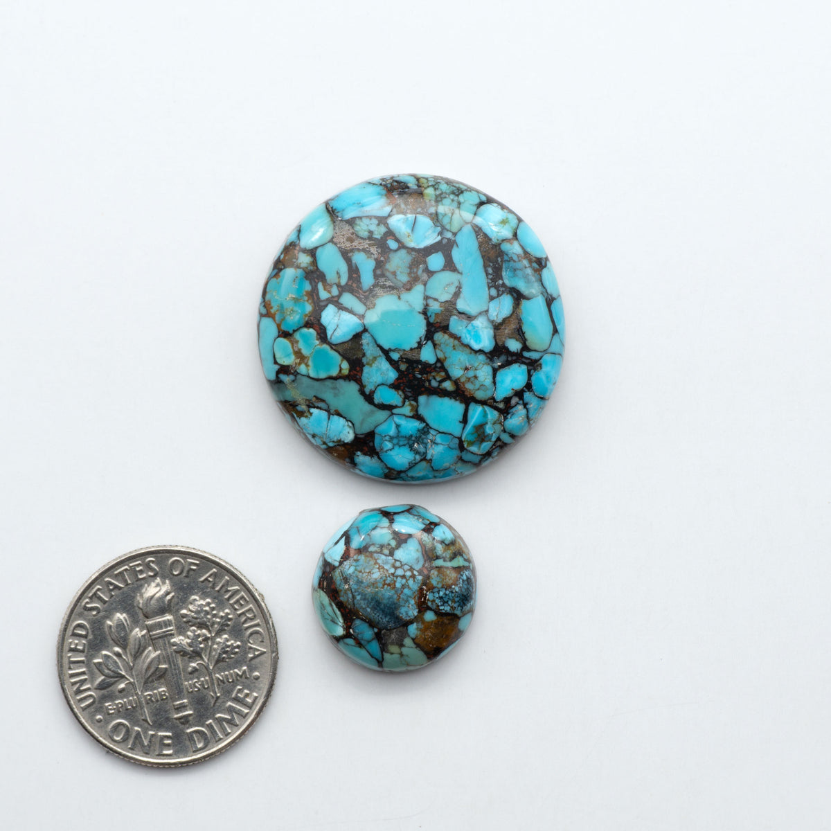 Pressed Turquoise nugget cabochons, composite material with a blue color and dark matrix on a white background, with a US dime for scale.
