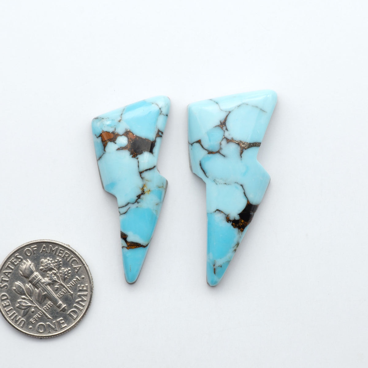 Pressed Turquoise nugget cabochons, composite material with a blue color and dark matrix on a white background, with a US dime for scale.