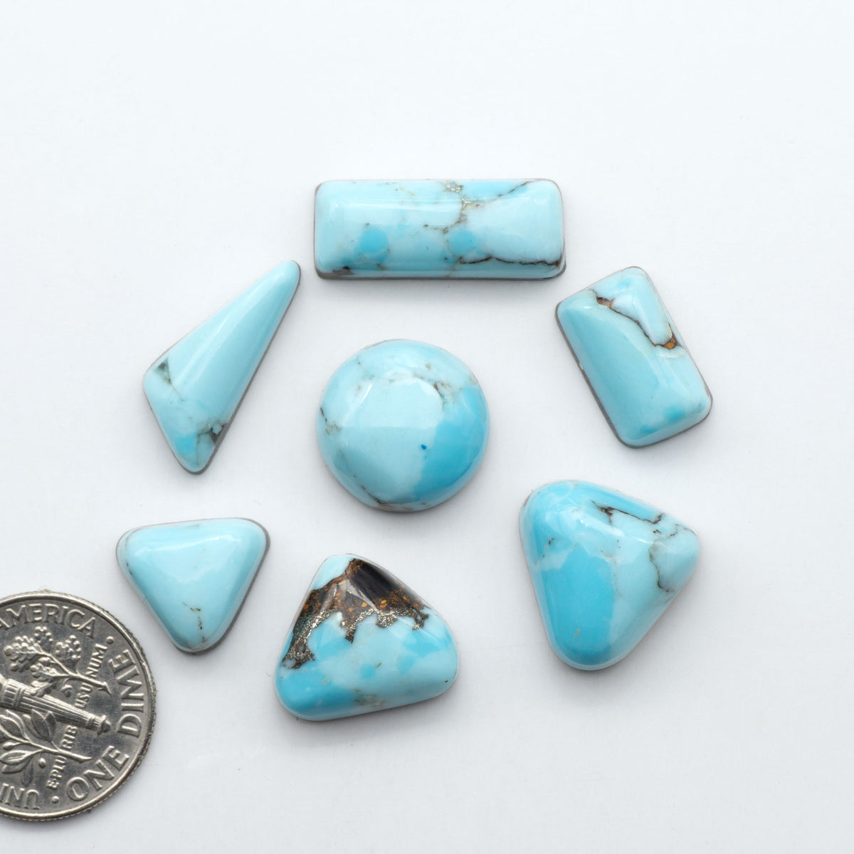 Pressed Turquoise nugget cabochons, composite material with a blue color and dark matrix on a white background, with a US dime for scale.