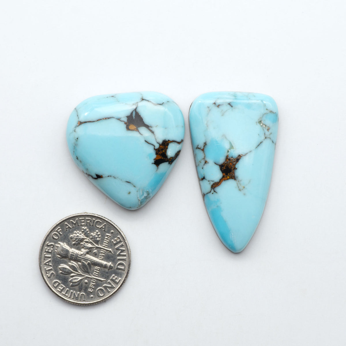 Pressed Turquoise nugget cabochons, composite material with a blue color and dark matrix on a white background, with a US dime for scale.