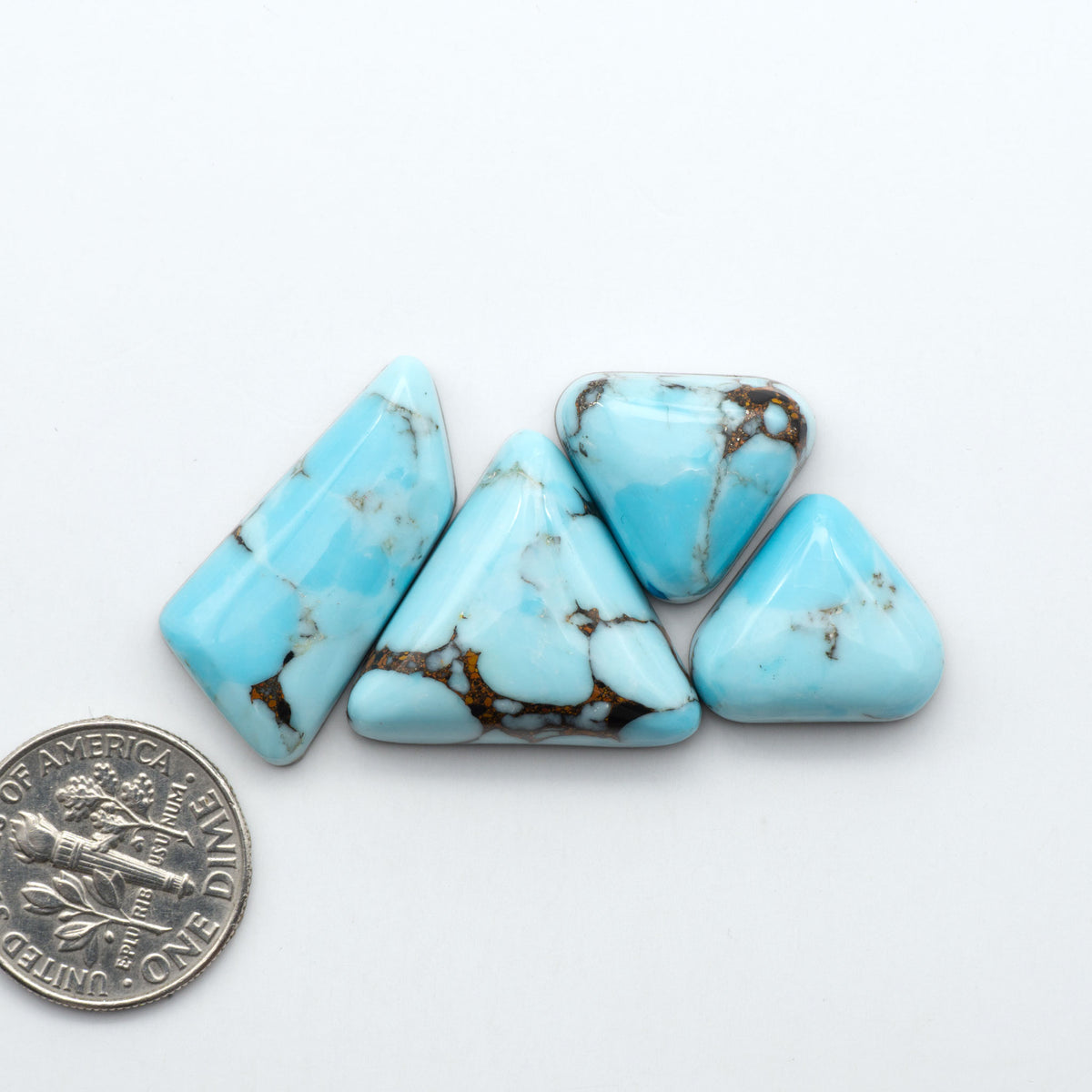 Pressed Turquoise nugget cabochons, composite material with a blue color and dark matrix on a white background, with a US dime for scale.