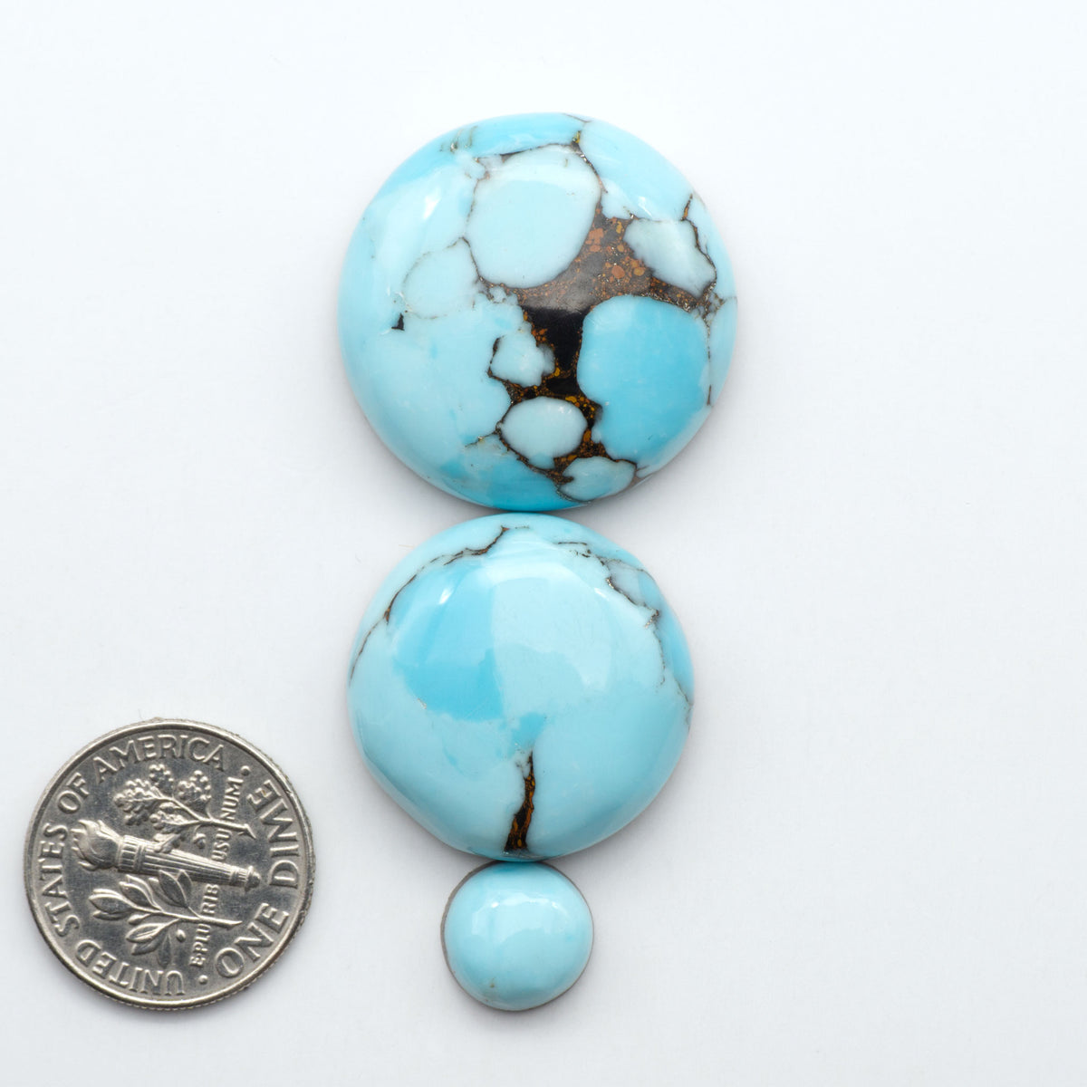 Pressed Turquoise nugget cabochons, composite material with a blue color and dark matrix on a white background, with a US dime for scale.