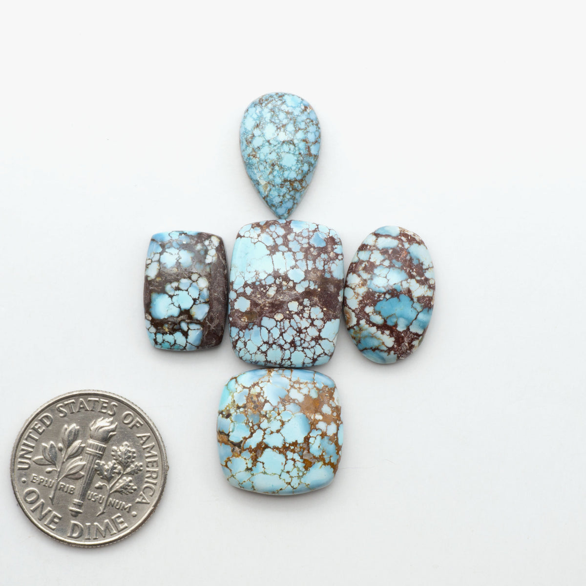 Golden Hills Turquoise cabochons, icy blue to lavender tones with chocolate matrix, polished stones on a white background with a US dime for scale