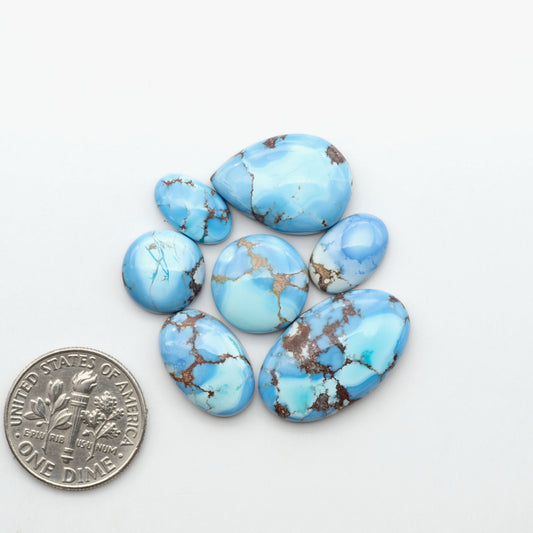 Golden Hills Turquoise cabochons, icy blue to lavender tones with chocolate matrix, polished stones on a white background with a US dime for scale