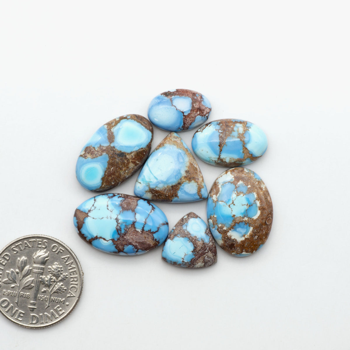 Golden Hills Turquoise cabochons, icy blue to lavender tones with chocolate matrix, polished stones on a white background with a US dime for scale