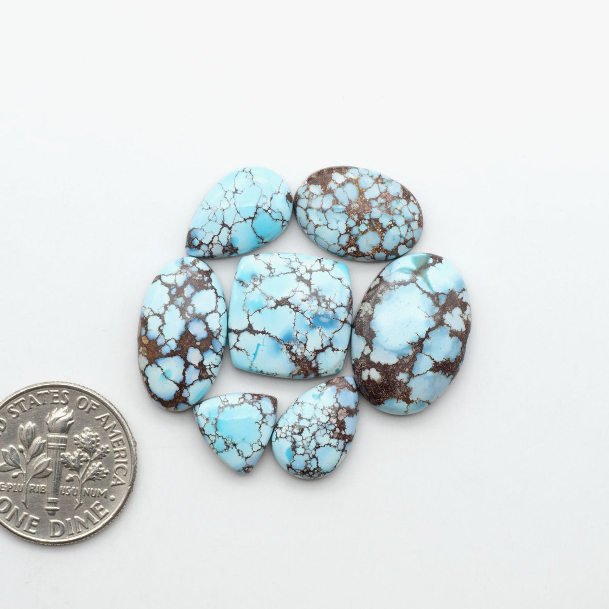 Golden Hills Turquoise cabochons, icy blue to lavender tones with chocolate matrix, polished stones on a white background with a US dime for scale