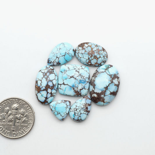 Golden Hills Turquoise cabochons, icy blue to lavender tones with chocolate matrix, polished stones on a white background with a US dime for scale
