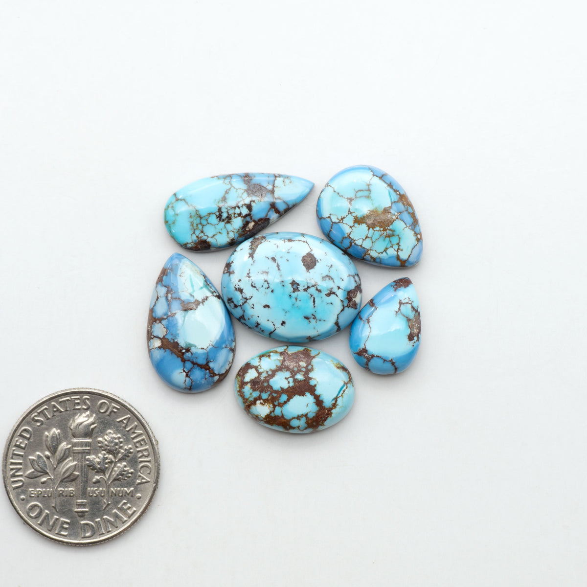 Golden Hills Turquoise cabochons, icy blue to lavender tones with chocolate matrix, polished stones on a white background with a US dime for scale