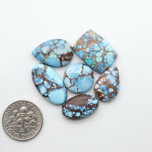 Golden Hills Turquoise cabochons, icy blue to lavender tones with chocolate matrix, polished stones on a white background with a US dime for scale