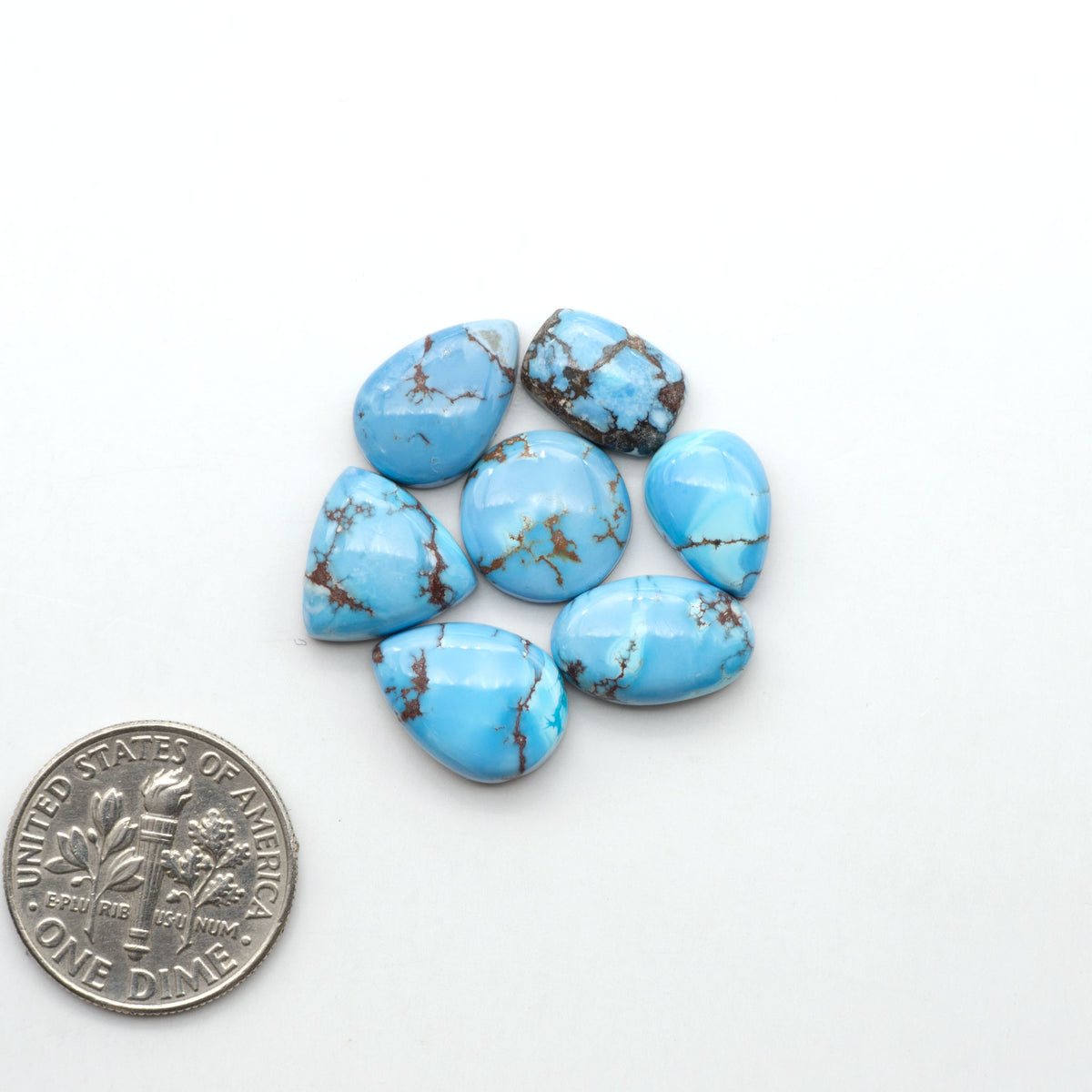 Golden Hills Turquoise cabochons, icy blue to lavender tones with chocolate matrix, polished stones on a white background with a US dime for scale
