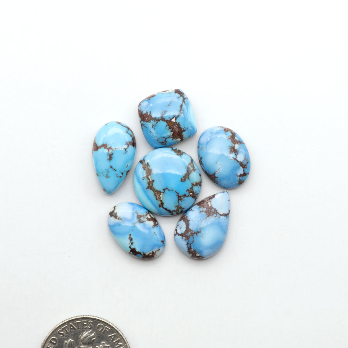 Golden Hills Turquoise cabochons, icy blue to lavender tones with chocolate matrix, polished stones on a white background with a US dime for scale
