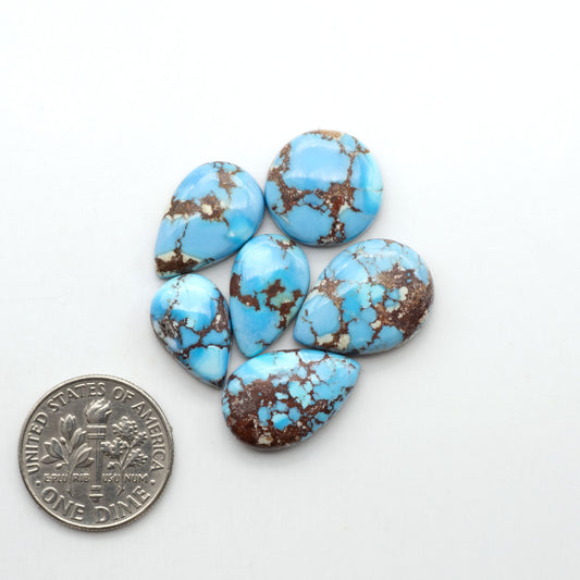 Golden Hills Turquoise cabochons, icy blue to lavender tones with chocolate matrix, polished stones on a white background with a US dime for scale