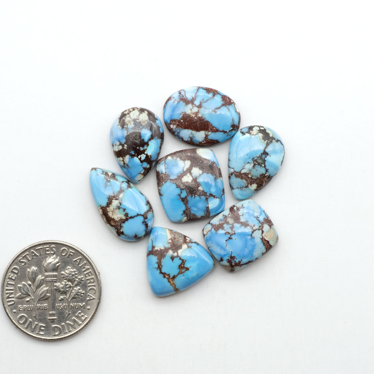 Golden Hills Turquoise cabochons, icy blue to lavender tones with chocolate matrix, polished stones on a white background with a US dime for scale