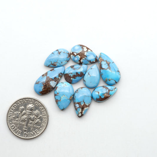 Golden Hills Turquoise cabochons, icy blue to lavender tones with chocolate matrix, polished stones on a white background with a US dime for scale