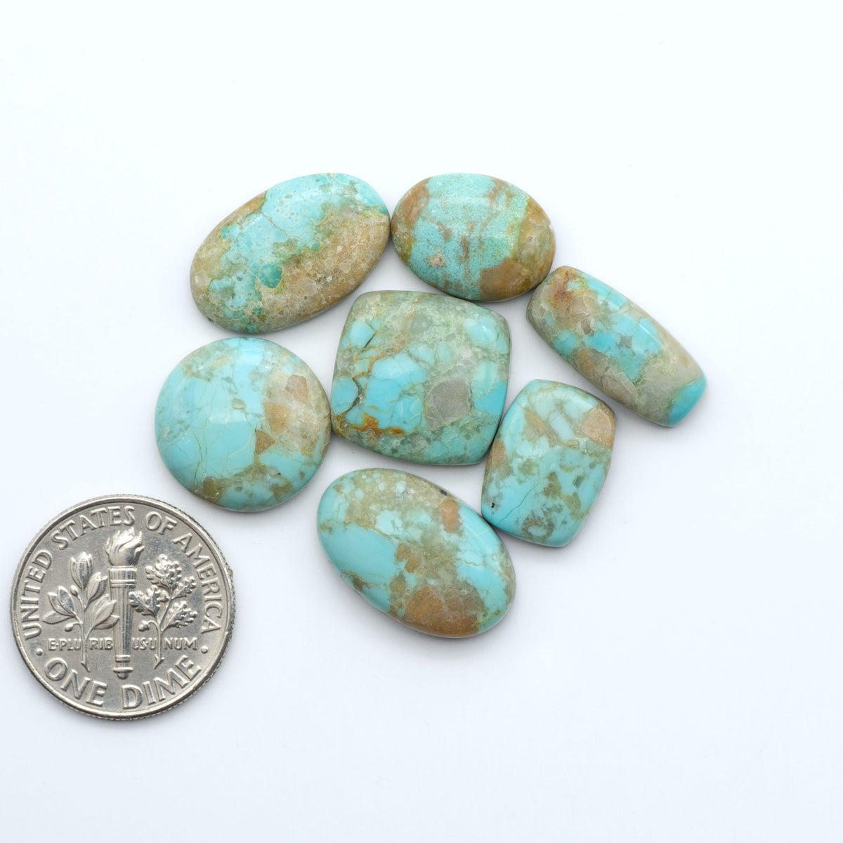 Pilot Mountain Turquoise cabochons, blue-green gemstones with natural matrix on a white background with a US dime for scale