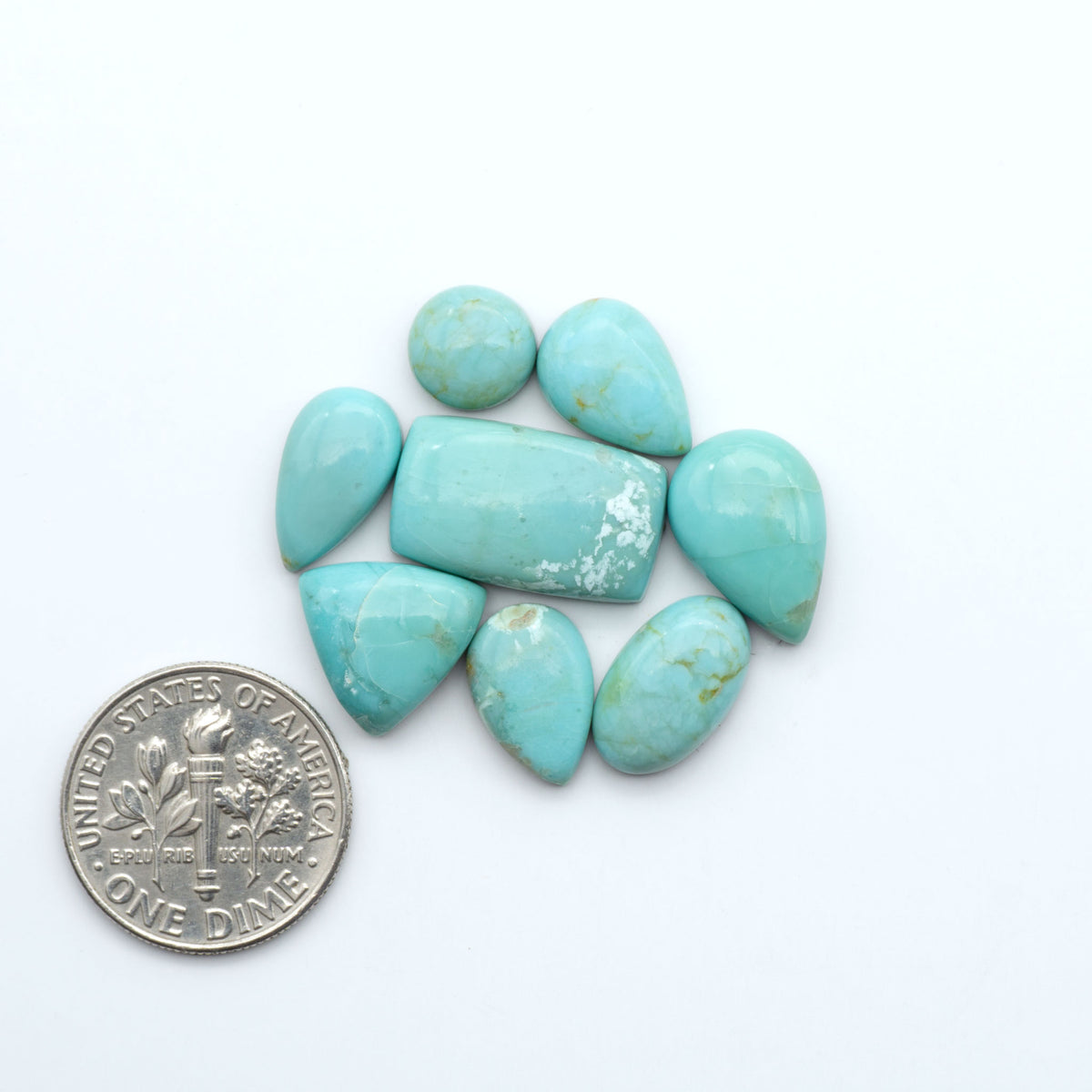 Pilot Mountain Turquoise cabochons, blue-green gemstones with natural matrix on a white background with a US dime for scale