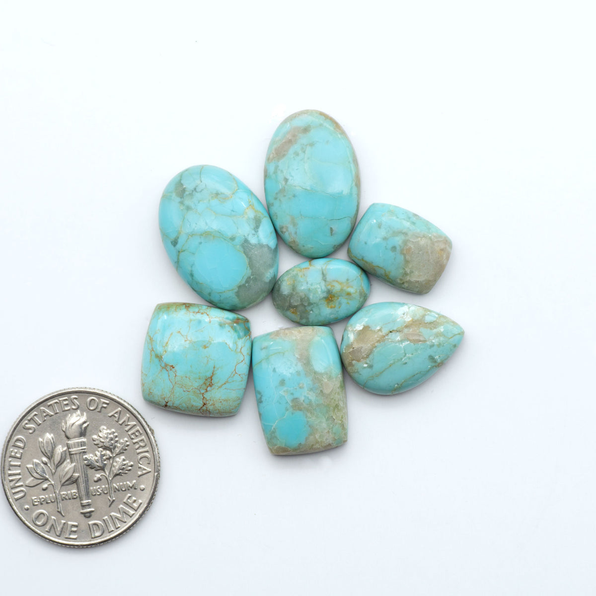 Pilot Mountain Turquoise cabochons, blue-green gemstones with natural matrix on a white background with a US dime for scale