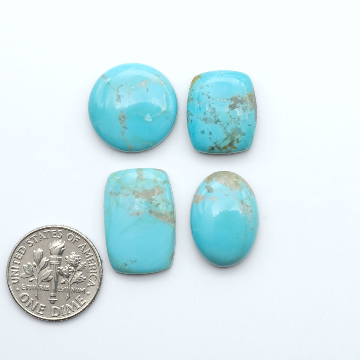 Pilot Mountain Turquoise cabochons, blue-green gemstones with natural matrix on a white background with a US dime for scale