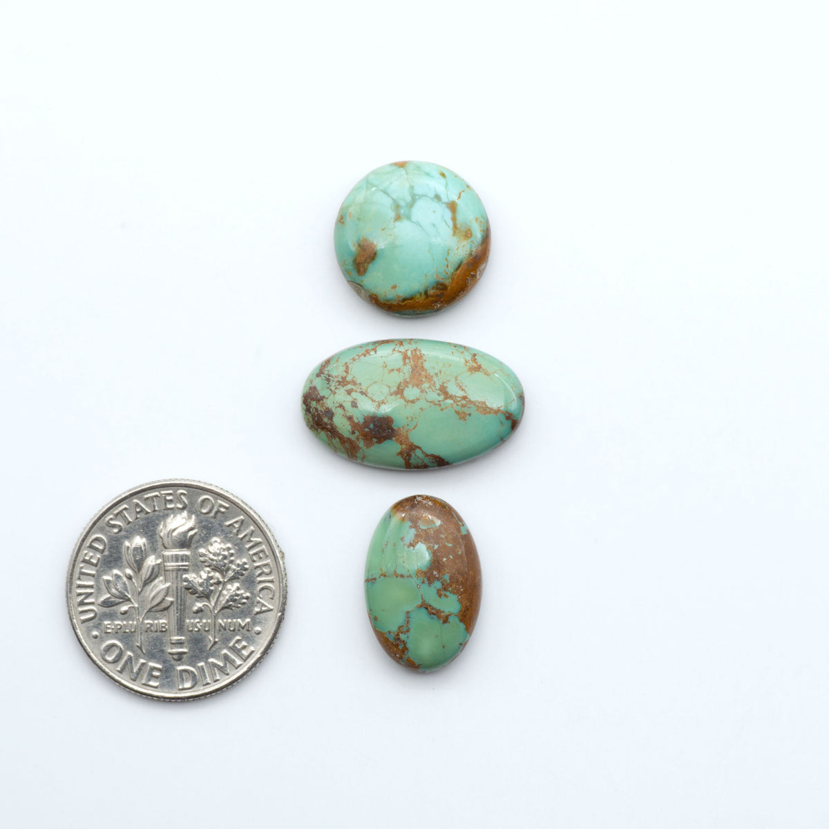 Pilot Mountain Turquoise cabochons, blue-green gemstones with natural matrix on a white background with a US dime for scale