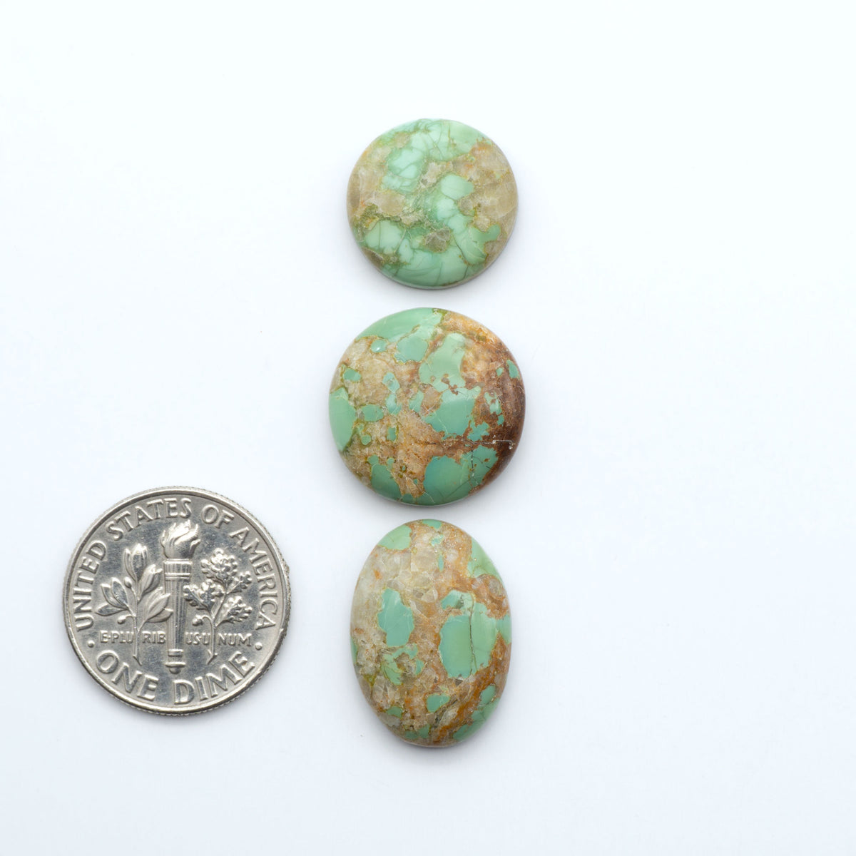 Pilot Mountain Turquoise cabochons, blue-green gemstones with natural matrix on a white background with a US dime for scale