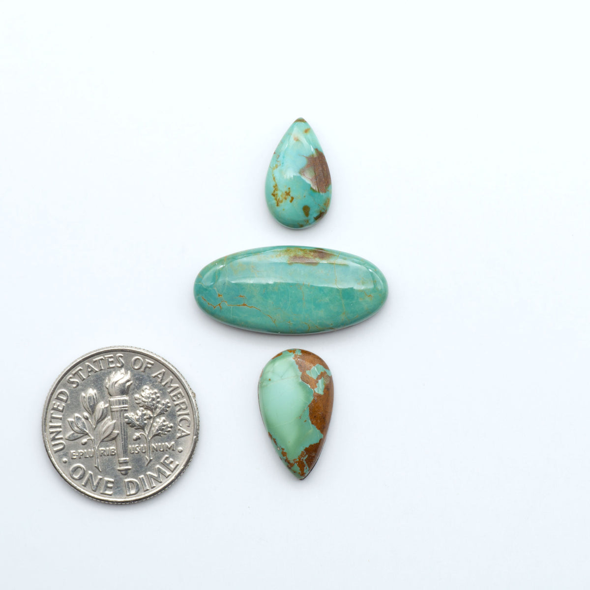 Pilot Mountain Turquoise cabochons, blue-green gemstones with natural matrix on a white background with a US dime for scale
