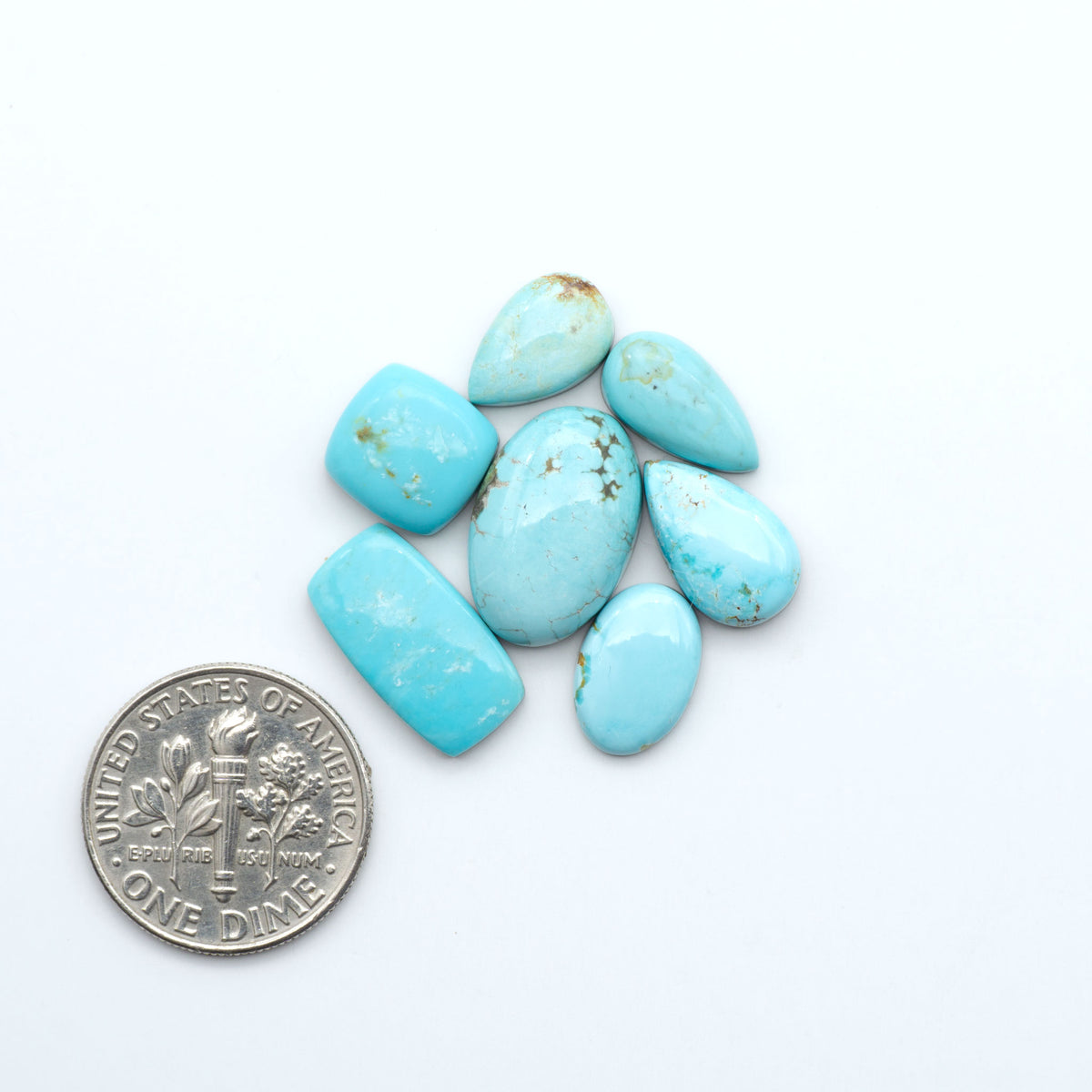 Kings Manassa Turquoise cabochons, polished green-blue gemstones with natural matrix on a white background with a US dime for scale