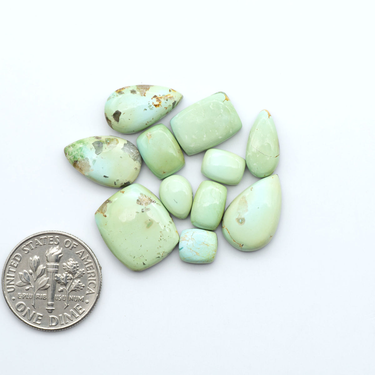 Sonoran Mountain Turquoise cabochons, blue-green color with natural matrix, polished stones on a white background, with a US dime for scale